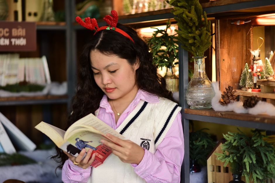 Cô gái tập trung đọc sách bên kệ trang trí Đọc sách chủ động giúp loại bỏ ảo tưởng kiến thức hiệu quả